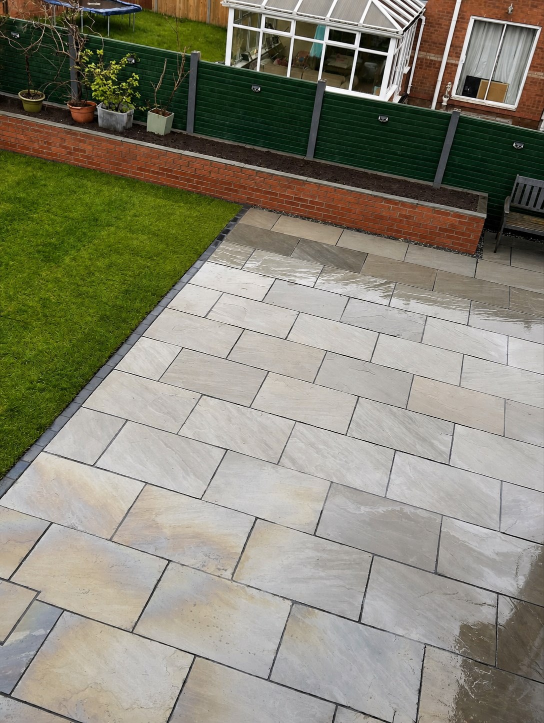 Detailed grey paving beside a lawn and brick planting bed
