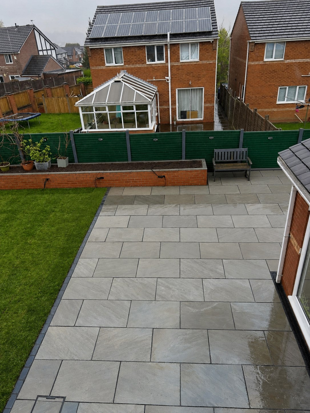 Grey paved patio, lawn and raised brick beds